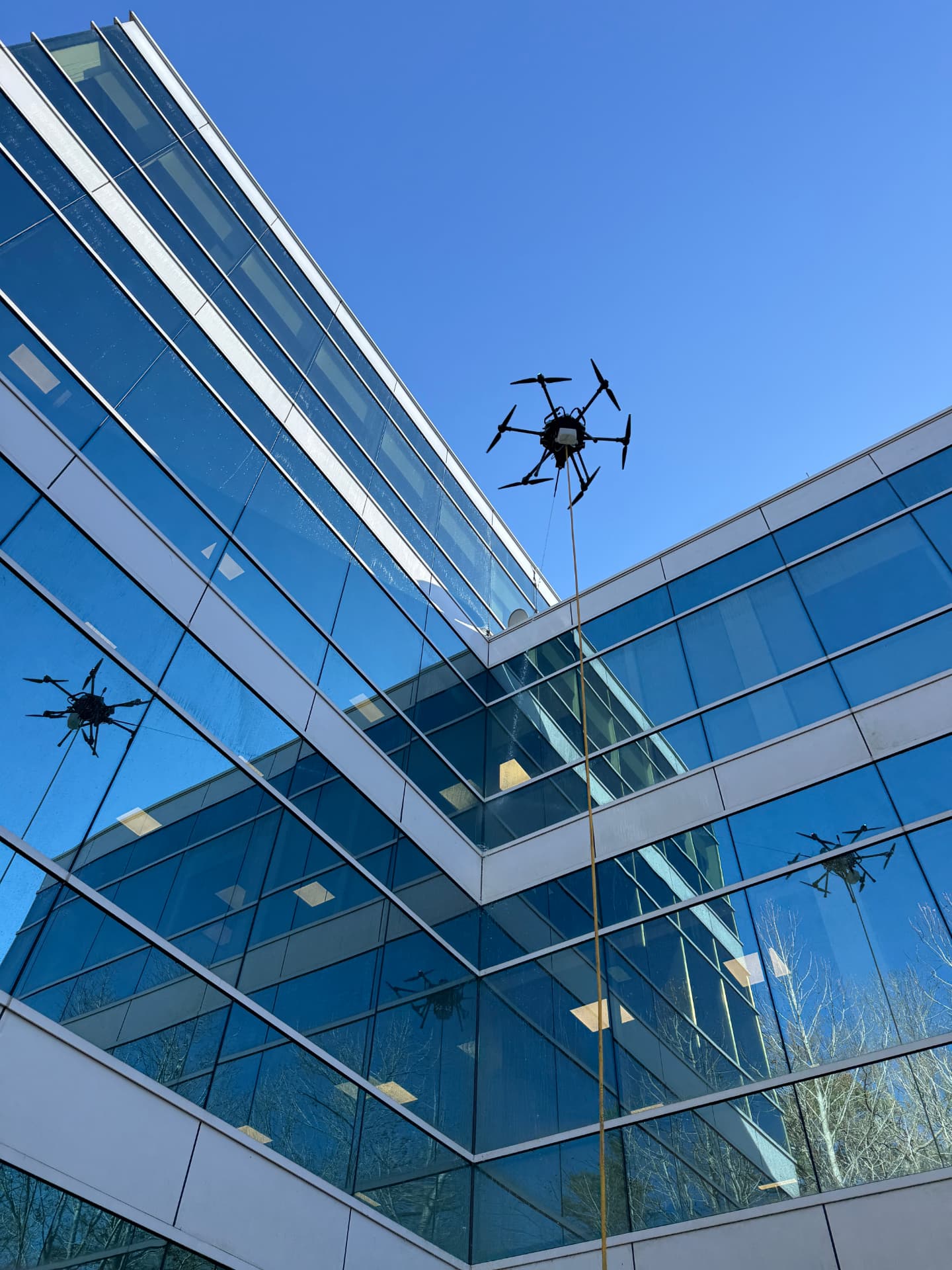 Cleaning drone in flight beside a glass atrium, reflected in the curtain wall
