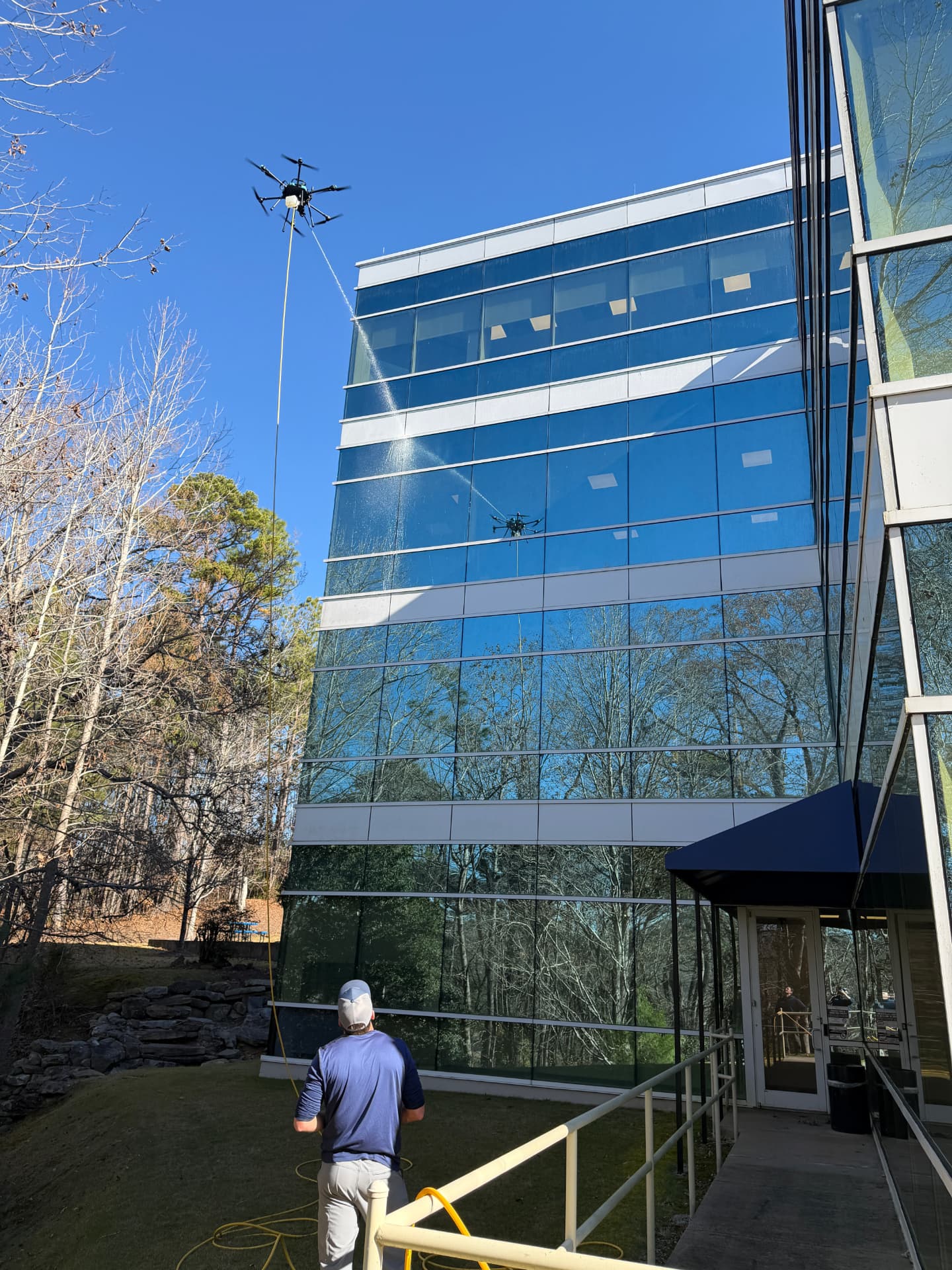 Operator on the ground guiding a drone rinsing an office tower facade