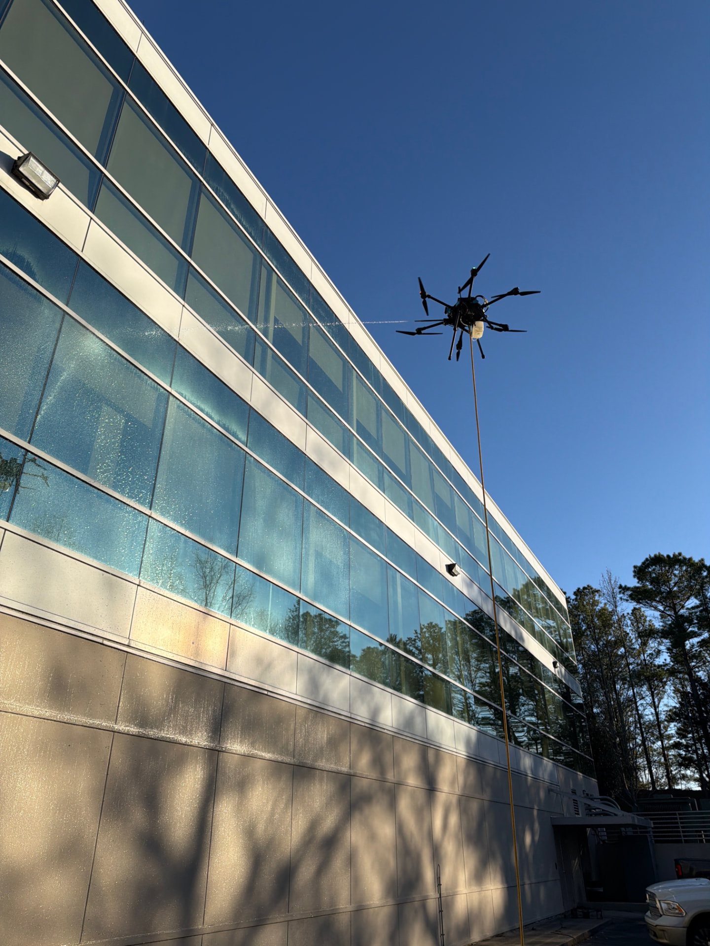 Drone spraying water across a glass and metal commercial facade