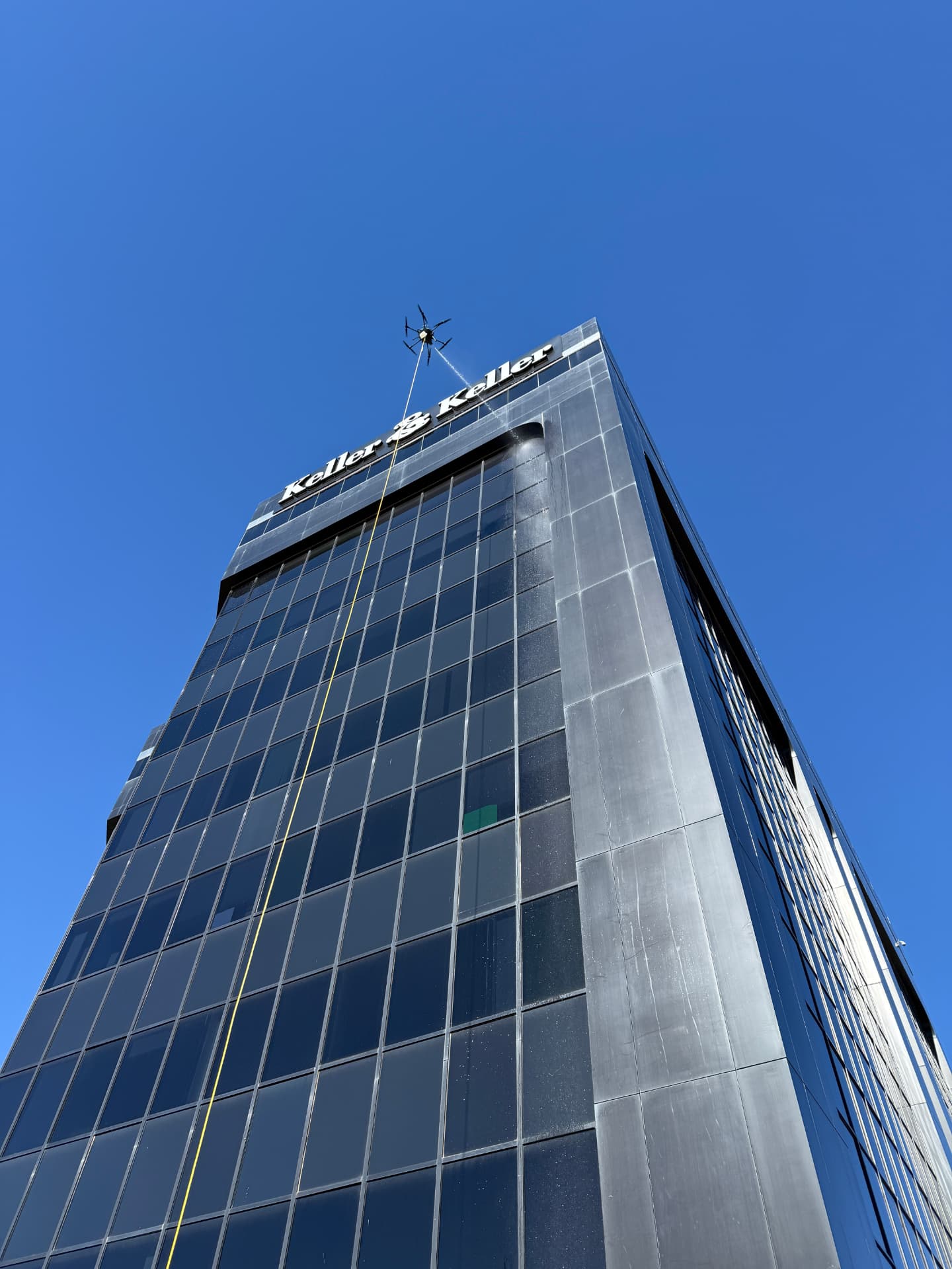 Drone cleaning the top floors of a dark glass high-rise tower