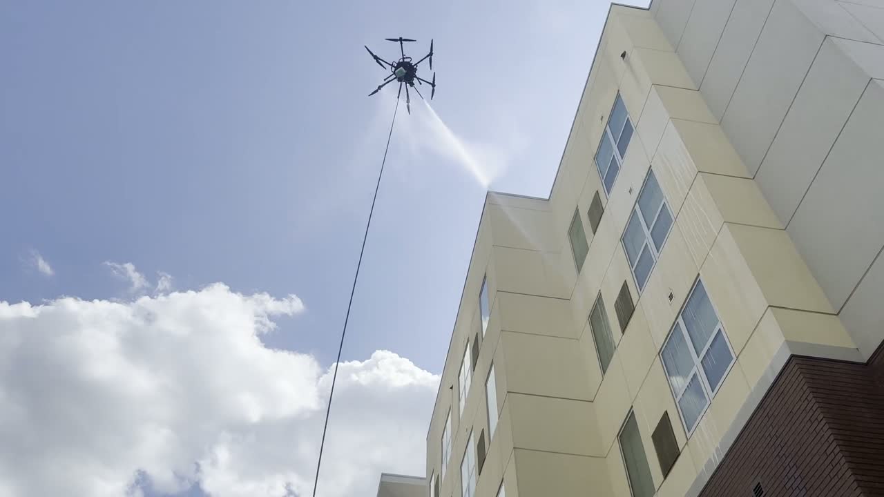 Drone soft washing the upper panels of a hotel exterior against a blue sky