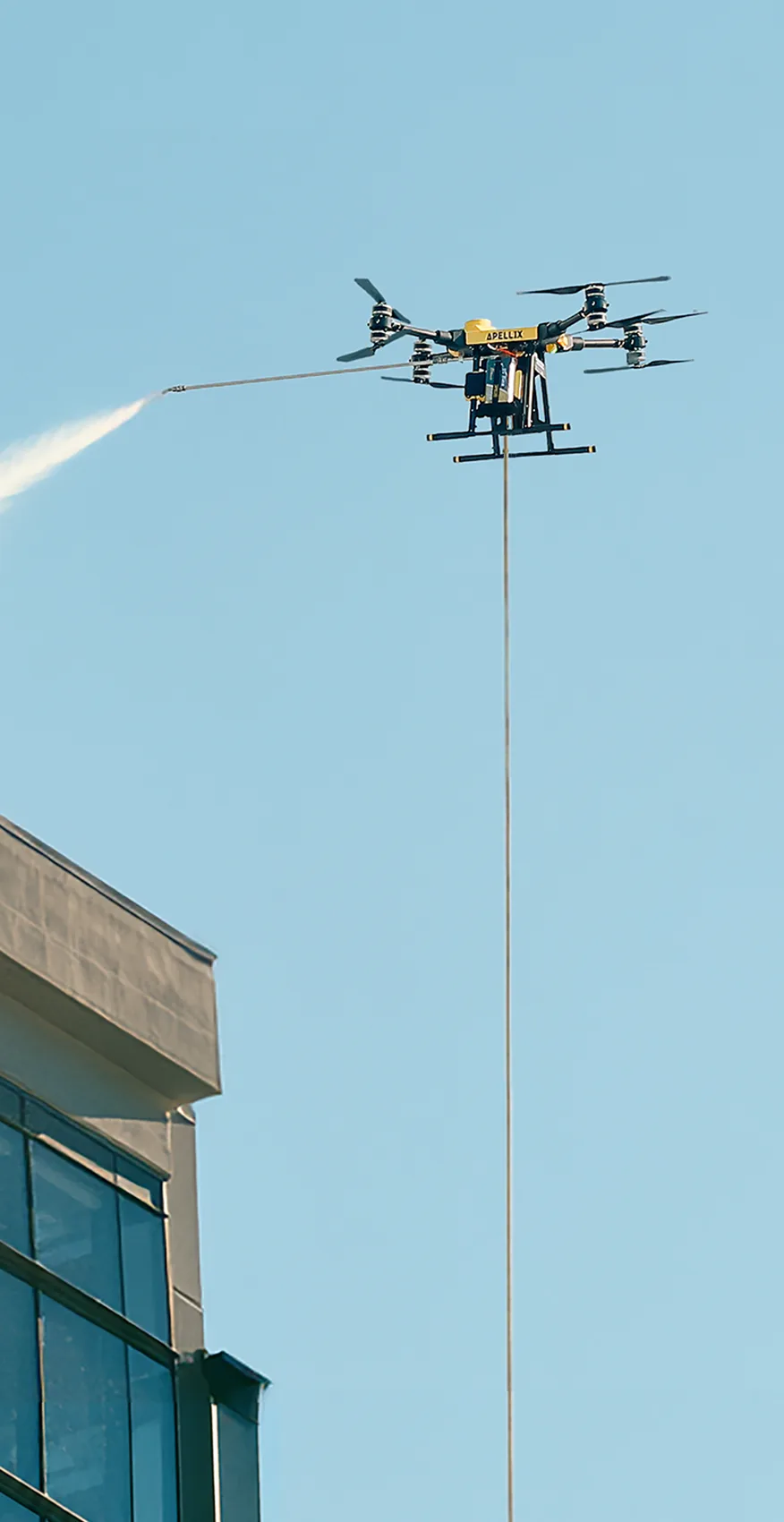 Apellix drone spraying water across the top of a glass commercial building