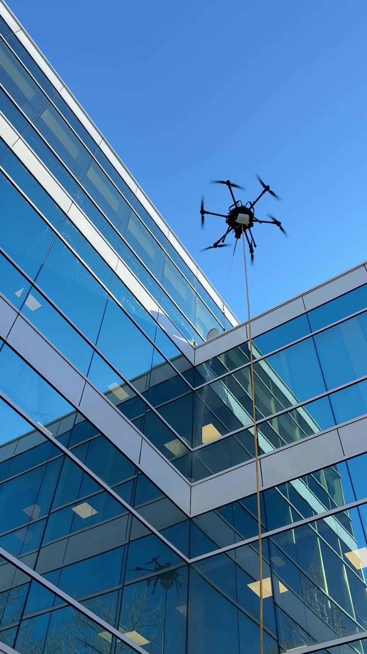 Drone cleaning a blue glass curtain wall from a courtyard angle